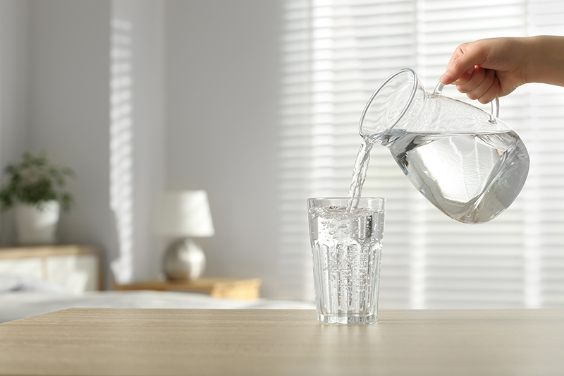 Woman pouring a glass of water from a jug to stay hydrated.