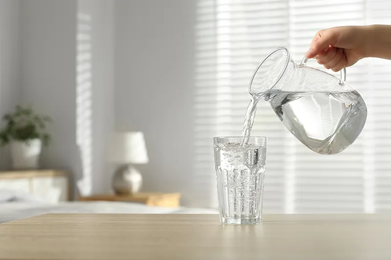 Woman pouring a glass of water from a jug to stay hydrated.